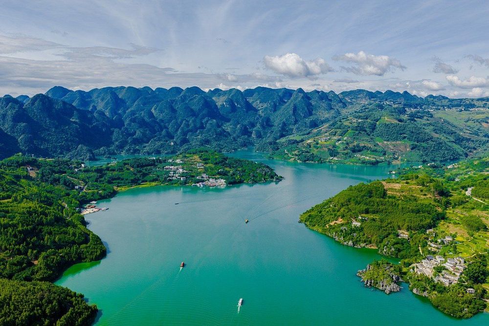 Lush green mountains surrounding a winding turquoise lake under a bright sky.