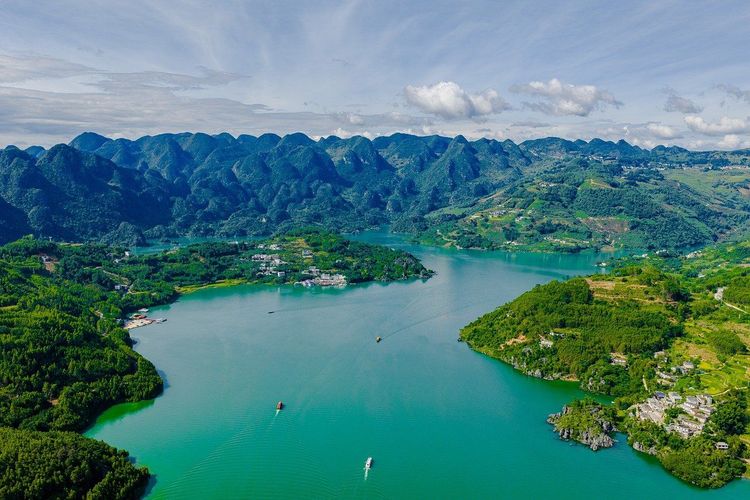 Lush green mountains surrounding a winding turquoise lake under a bright sky.